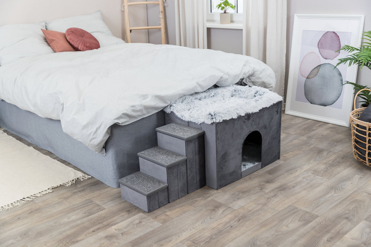 Graues Bett mit weißer Bettwäsche, daneben eine graue Höhle mit Treppe und flauschiger Oberfläche auf Holzfußboden.