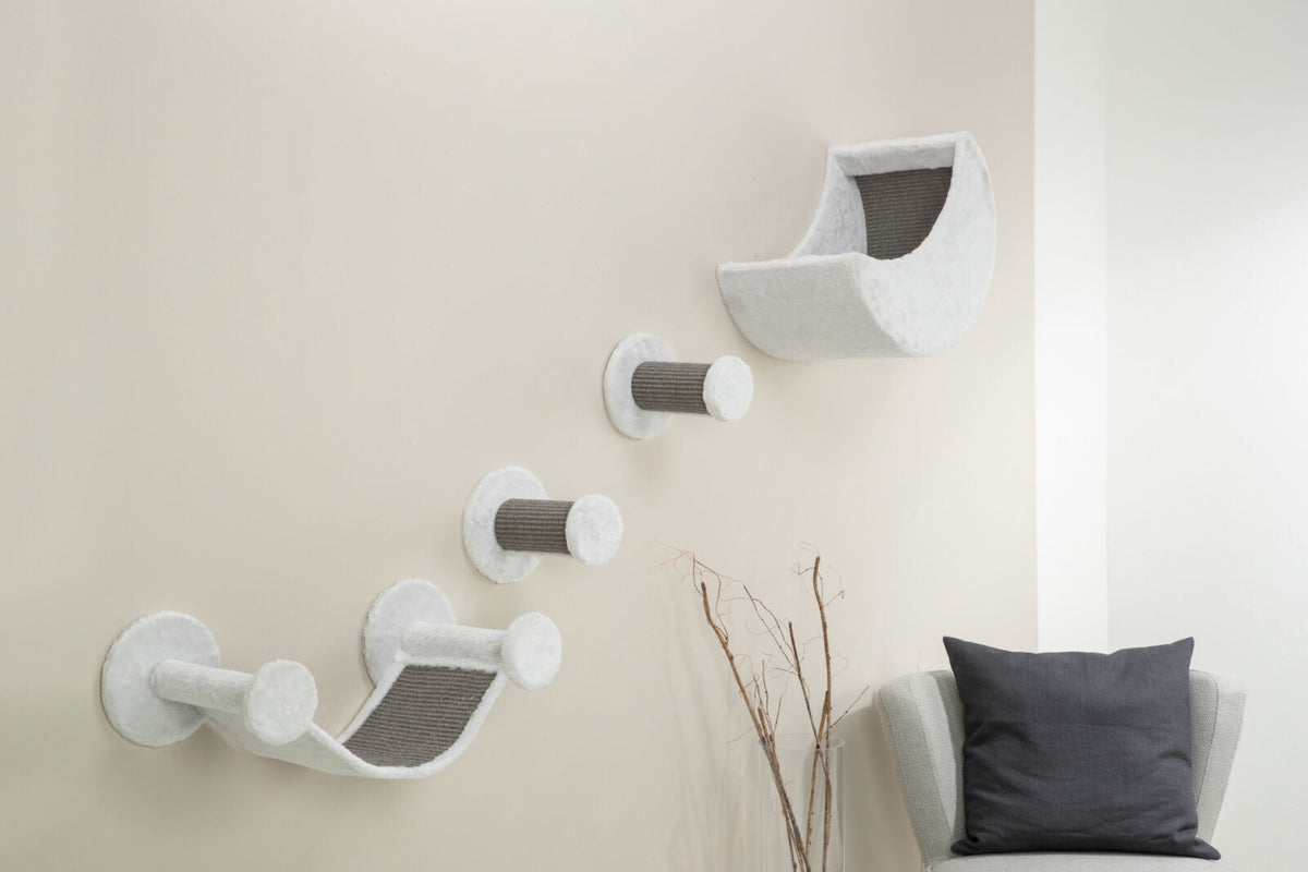 Weiße Wand mit montierter Kratzwand aus grauen Elementen und einer Liegefläche, daneben steht ein Sessel.