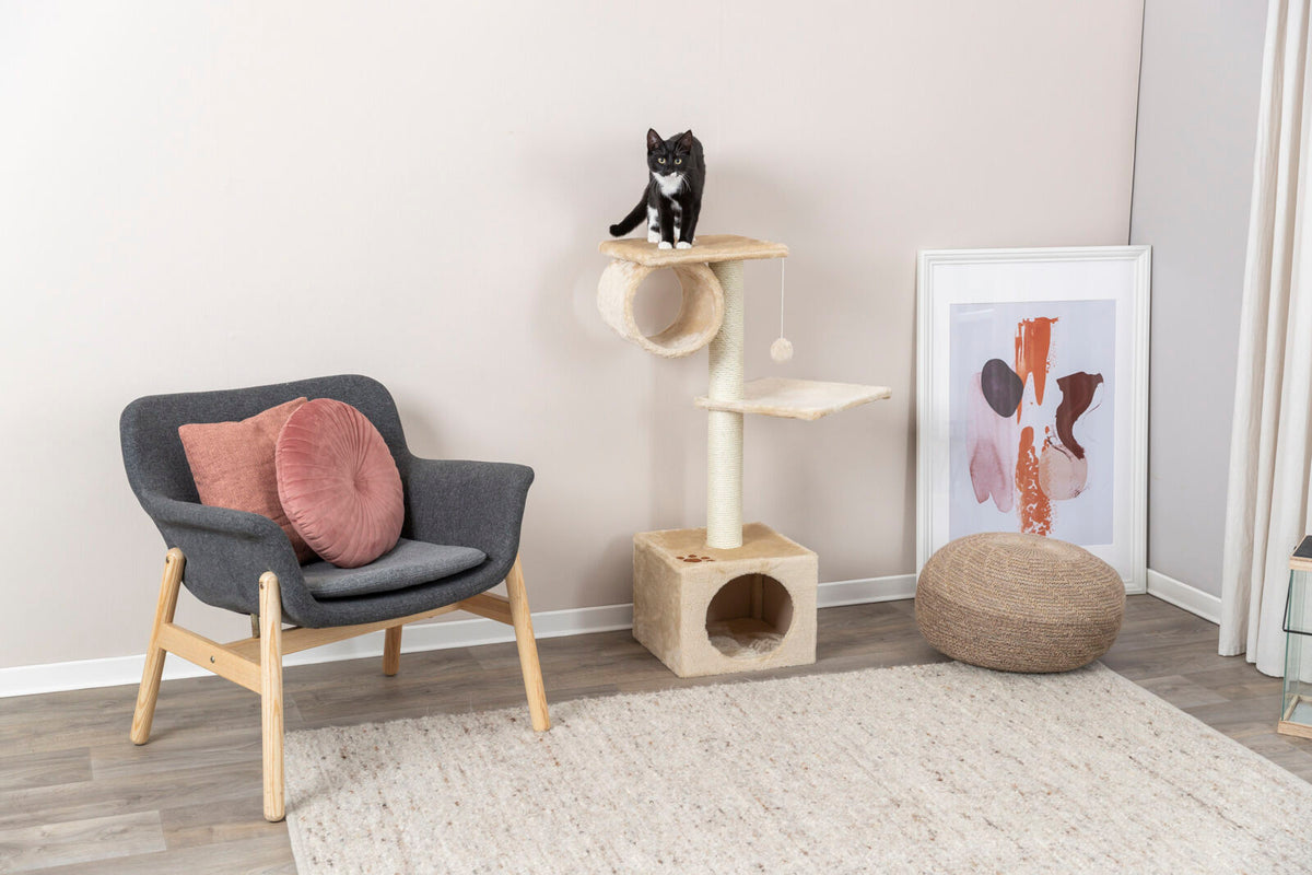 Katzenkratzbaum mit zwei Plattformen, auf dem eine schwarz-weiße Katze sitzt, daneben ein Sessel mit rosa Kissen.