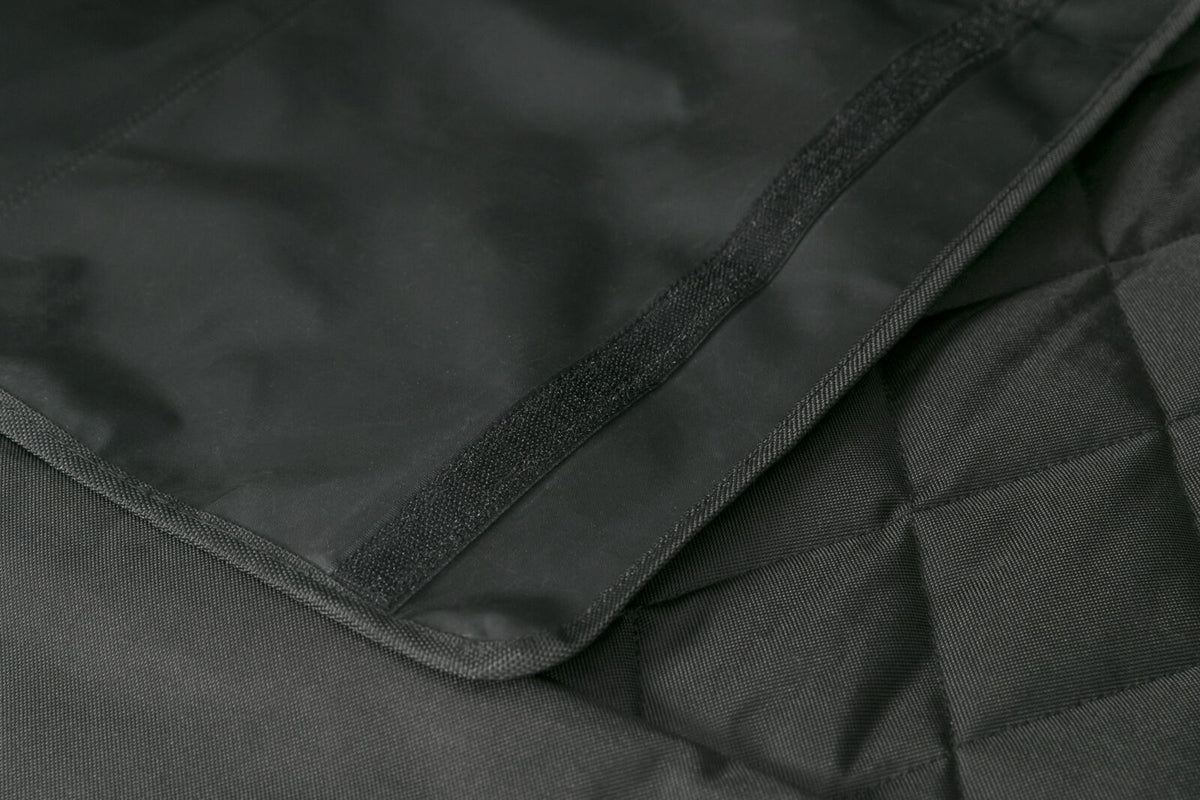Schwarzes gewebtes Material mit diagonal verlaufender Naht und Klettverschluss auf einer Oberfläche.