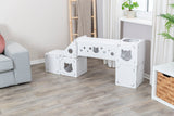 Weißes modulares Klettersystem mit Ausschnitten und Löchern, platziert auf hellem Holzfußboden neben grauem Sofa.
