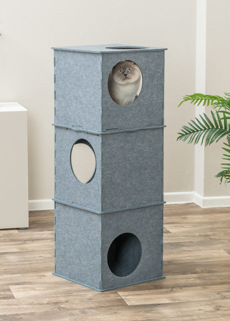 Grauer, dreistöckiger Turm mit kreisförmigen Öffnungen, eine Katze schaut aus der oberen Etage heraus, umgeben von Zimmerpflanzen.