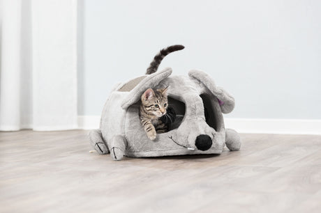Kleine Katze schaut aus einer grauen Plüschhöhle in Form einer Maus auf hellem Holzboden hervor.