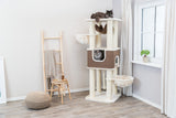 Katzenkratzbaum mit zwei Katzen, Stehleiter mit Decke, Hocker und Glas, Fensterbank mit Pflanze, helle Raumgestaltung.