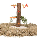 Holzpfosten mit Löchern und Zweigen, an dem orangefarbene und rote Gemüse- und Fruchtstücke angebracht sind, auf einer Basis aus Stroh.
