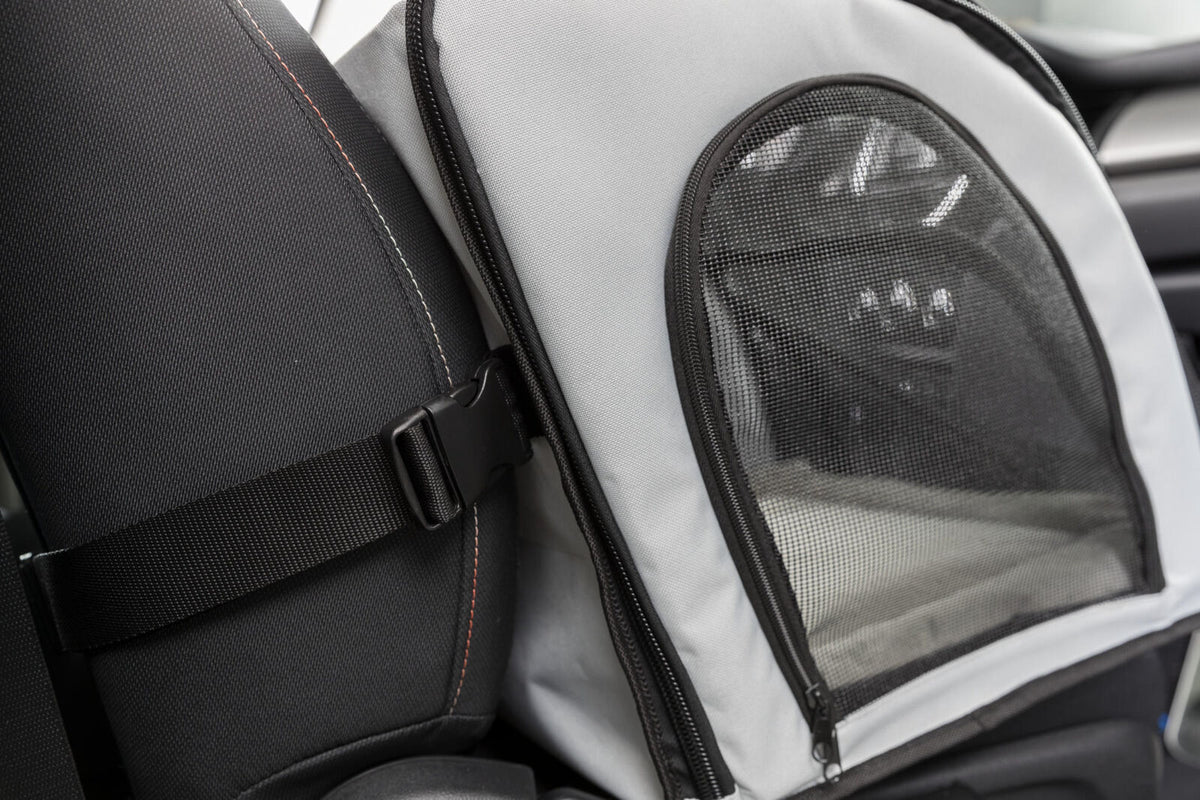 Grau-schwarzes Transportgerät im Auto, mit Netzfenster und Gurt an der Rückenlehne befestigt.