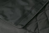 Schwarzes gewebtes Material mit diagonal verlaufender Naht und Klettverschluss auf einer Oberfläche.