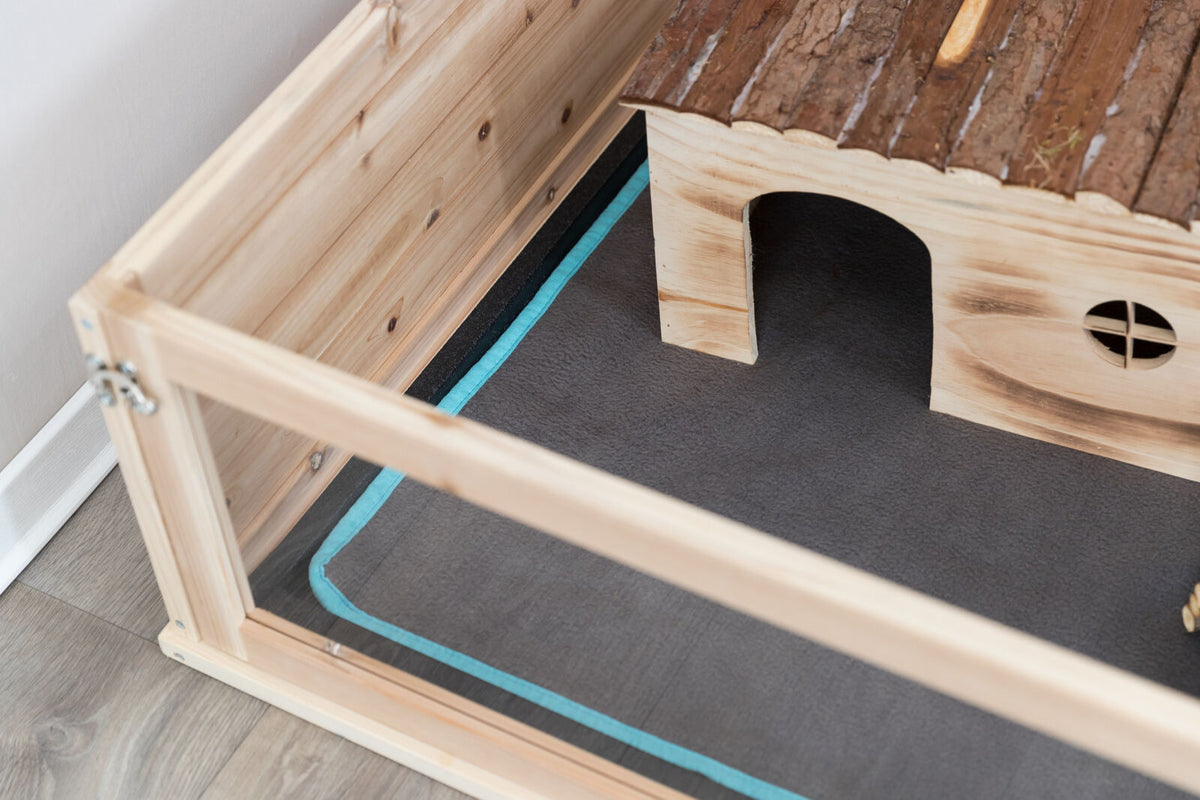 Holzgehäuse mit Streuunterlage und kleinem Haus, braun und blau, auf einem Holzboden.