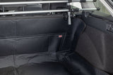 Schwarze Kofferraumauskleidung in einem Auto mit sichtbarem Schutzgitter und einem kleinen roten Etikett.
