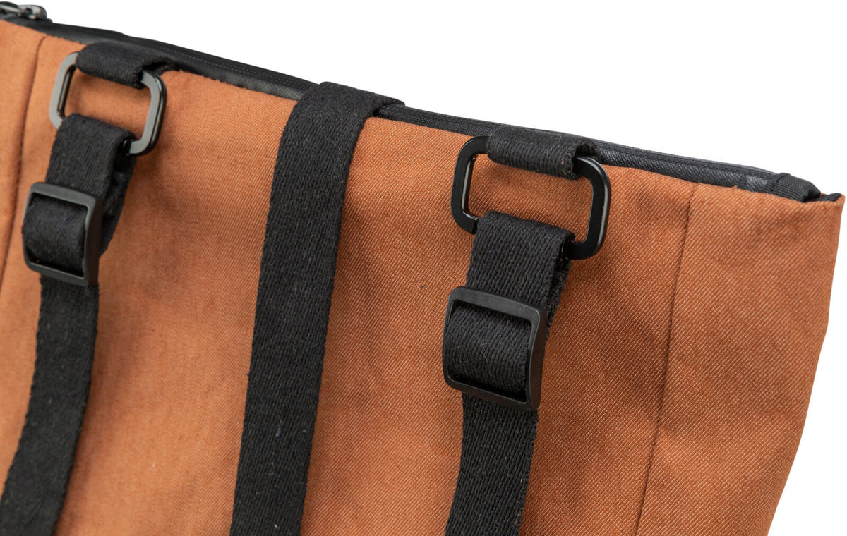 Nahaufnahme einer braunen Tasche aus Stoff mit zwei schwarzen Trägern und quadratischen Schnallen.