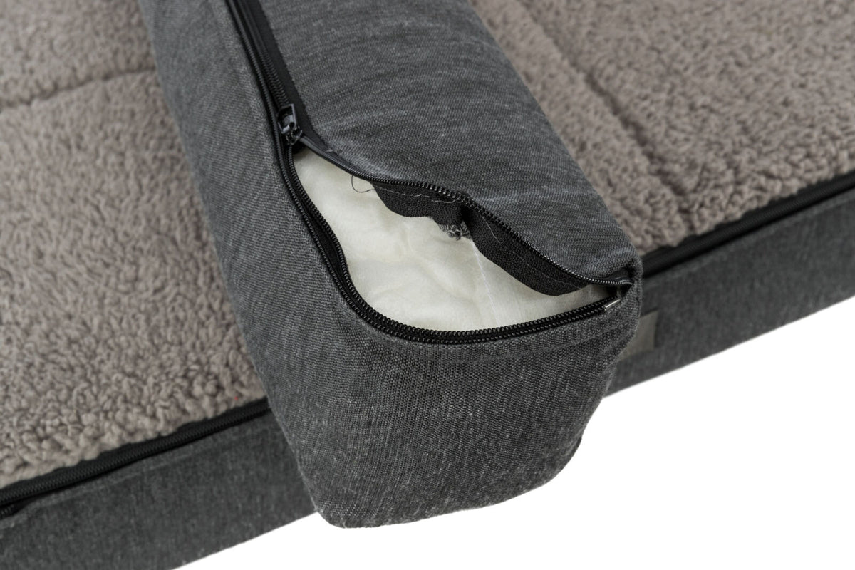 Graues Hundebett mit abnehmbarem Bezug, offenen Reisverschluss zeigend, und flauschiger, beige-weißer Oberfläche.