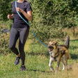Person joggt mit einem beige-braunen Hund an blauer Leine über eine Wiese.