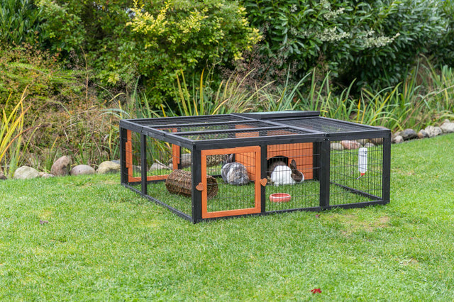 Kleintiergehege aus Metall mit Holzdetails auf grünem Rasen, innen zwei Kaninchen und Spielzeug.