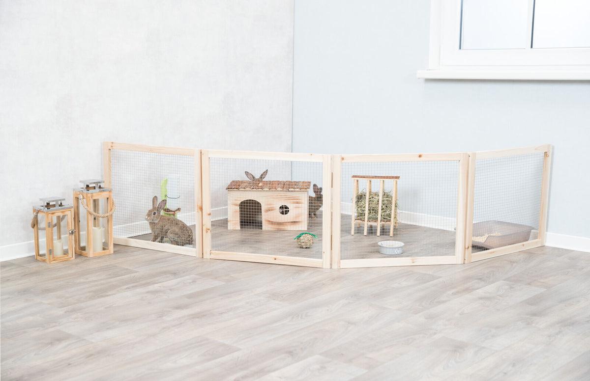 Holzgehege mit Kaninchen, Haus und Heuraufe auf hellem Holzboden, daneben drei Laternen mit Kerzen.