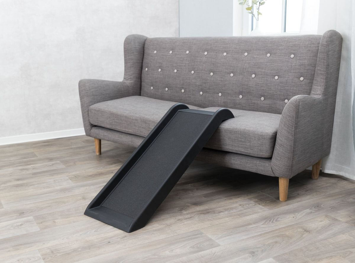 Graues Sofa mit Holzbeinen und gepolsterter Rückenlehne, davor eine schwarze Rampe auf hellem Holzboden.