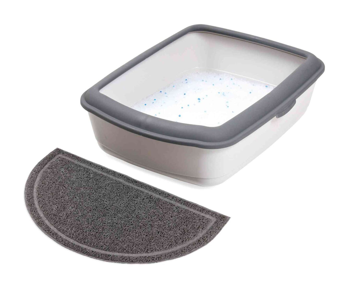 Offene Katzentoilette mit grauem Rand und Halbmond-Fußmatte, gefüllt mit weißem Streu.